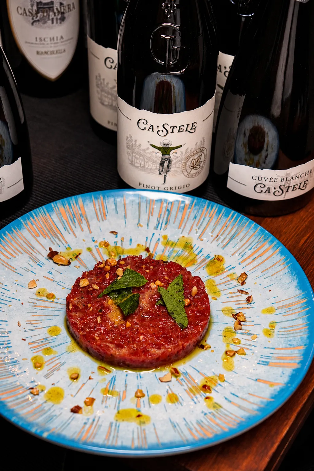 Tartare di Fassona con mandorle e menta davanti a bottiglie di vino